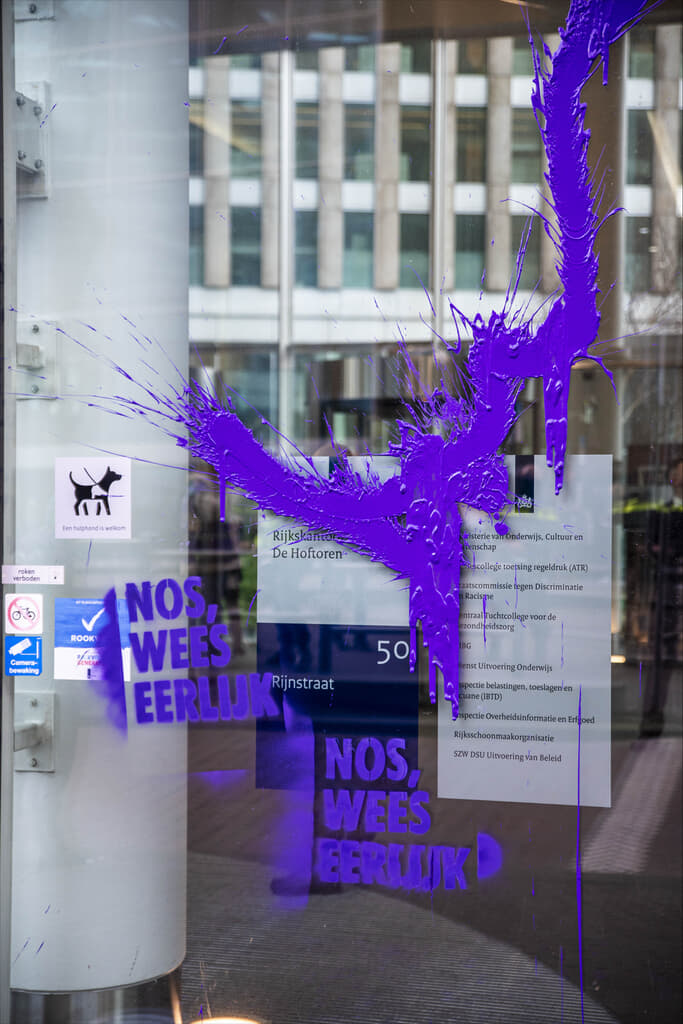 Raam met paarse verf en de tekst “NOS, Wees Eerlijk!” in krijtverf.