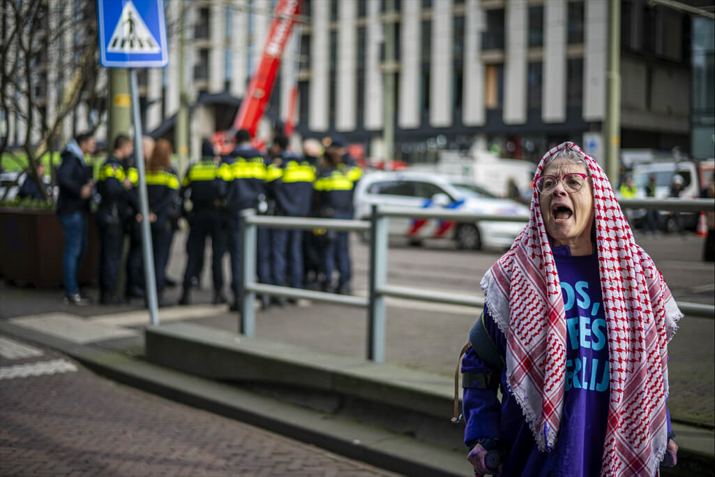 Roepende rebel met een keffiyeh over het hoofd met op de achtergrond een groep politieagenten.
